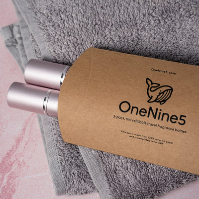 Two pink OneNine5 fragrance bottles poking out of the natural kraft paper packaging, resting on a towel in the bathroom