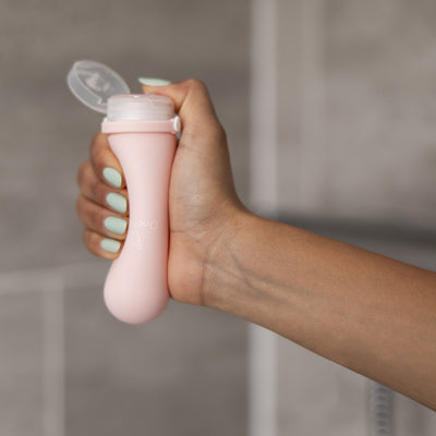 A female squeezing the soft silicone OneNine5 pink bottle in the palm of her hand, with the leakproof cap open.