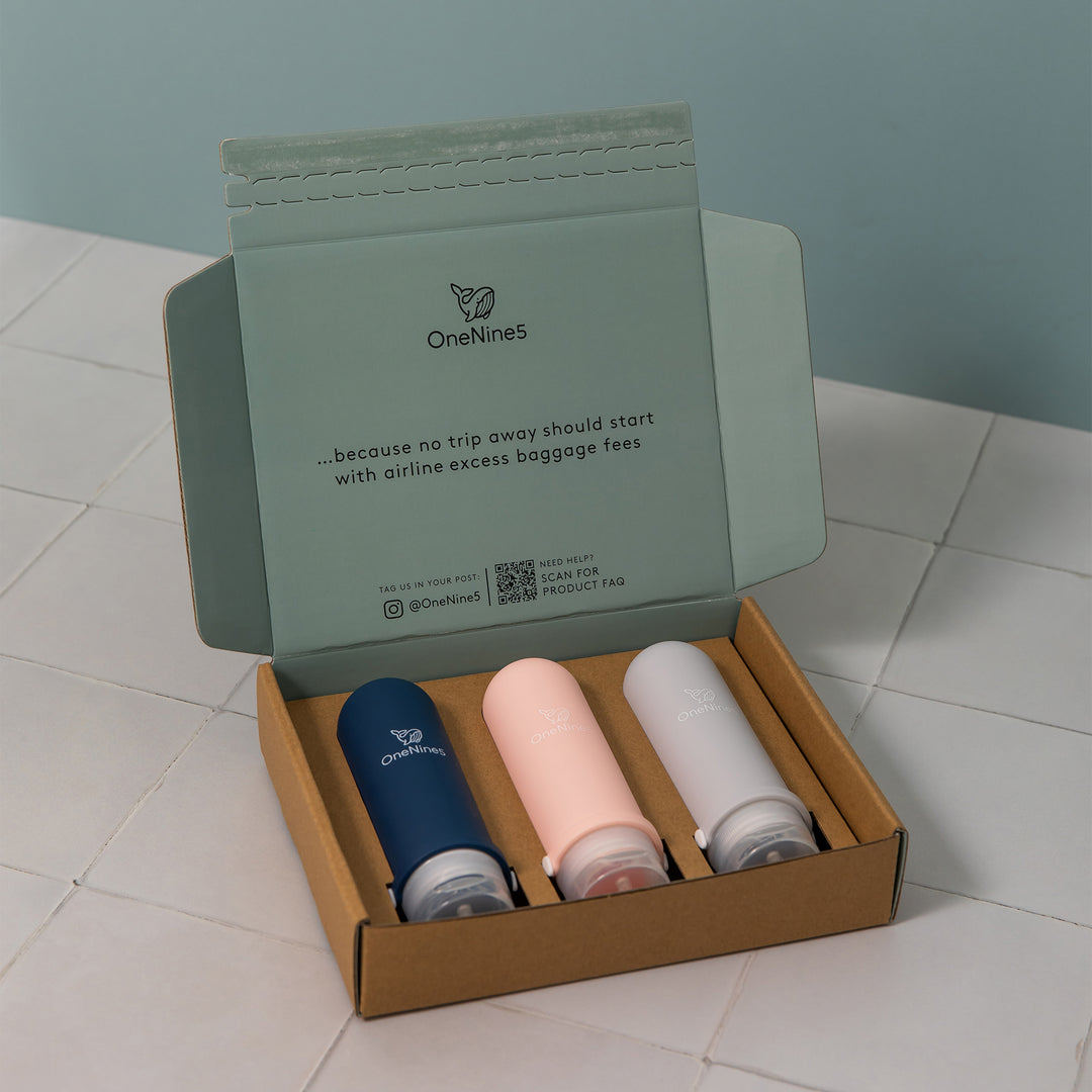 3 pack of mixed colour silicone travel bottles packed inside a brown, recyclable kraft paper box. Printed inside the packaging is the OneNine5 logo, a QR code and the caption ‘Because no trip away should start with airline excess baggage fees’.