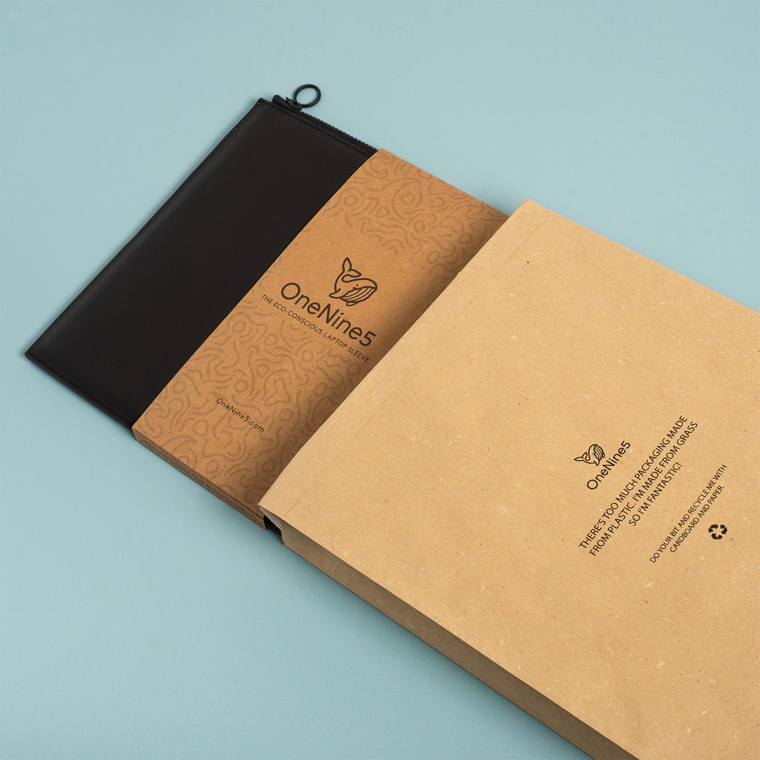 A Miho Black Laptop sleeve, with kraft paper packaging poking out the top of a OneNine5 branded grass mailer bag