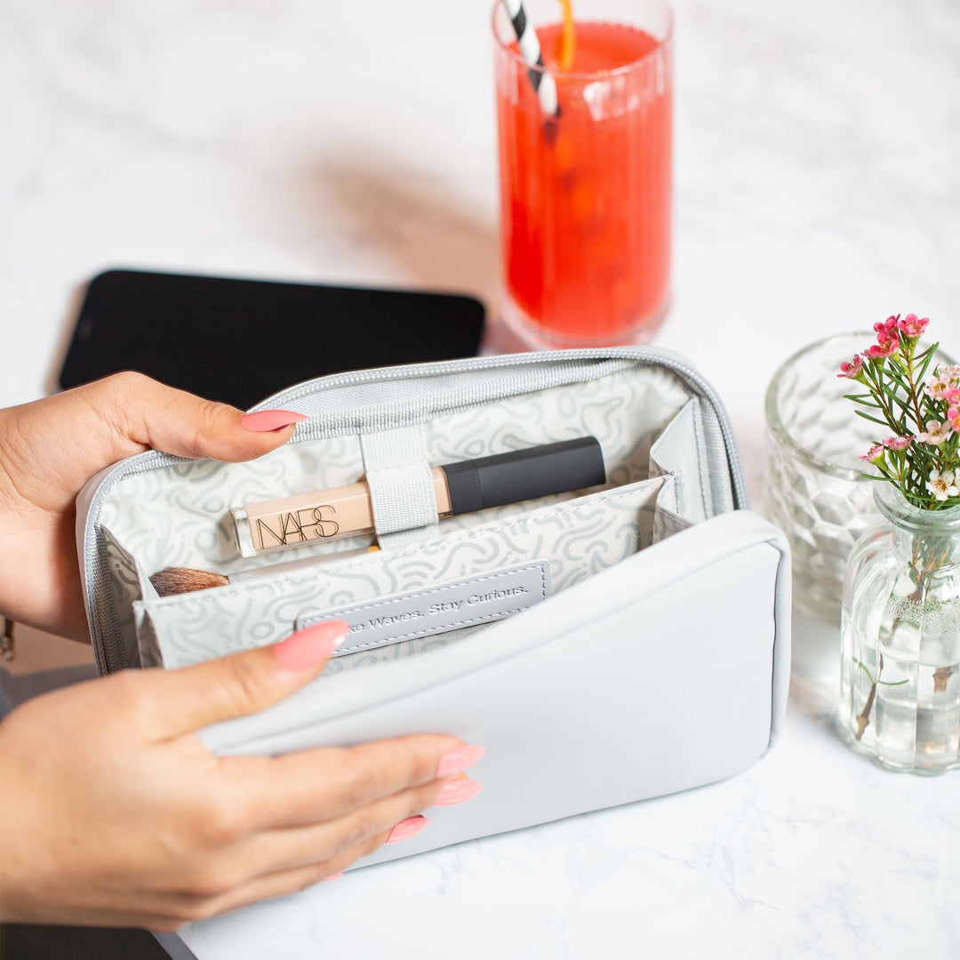 A woman opening the Moeraki Grey Eco Essentials Pouch in a restaurant, with a drink on the table. Inside the open