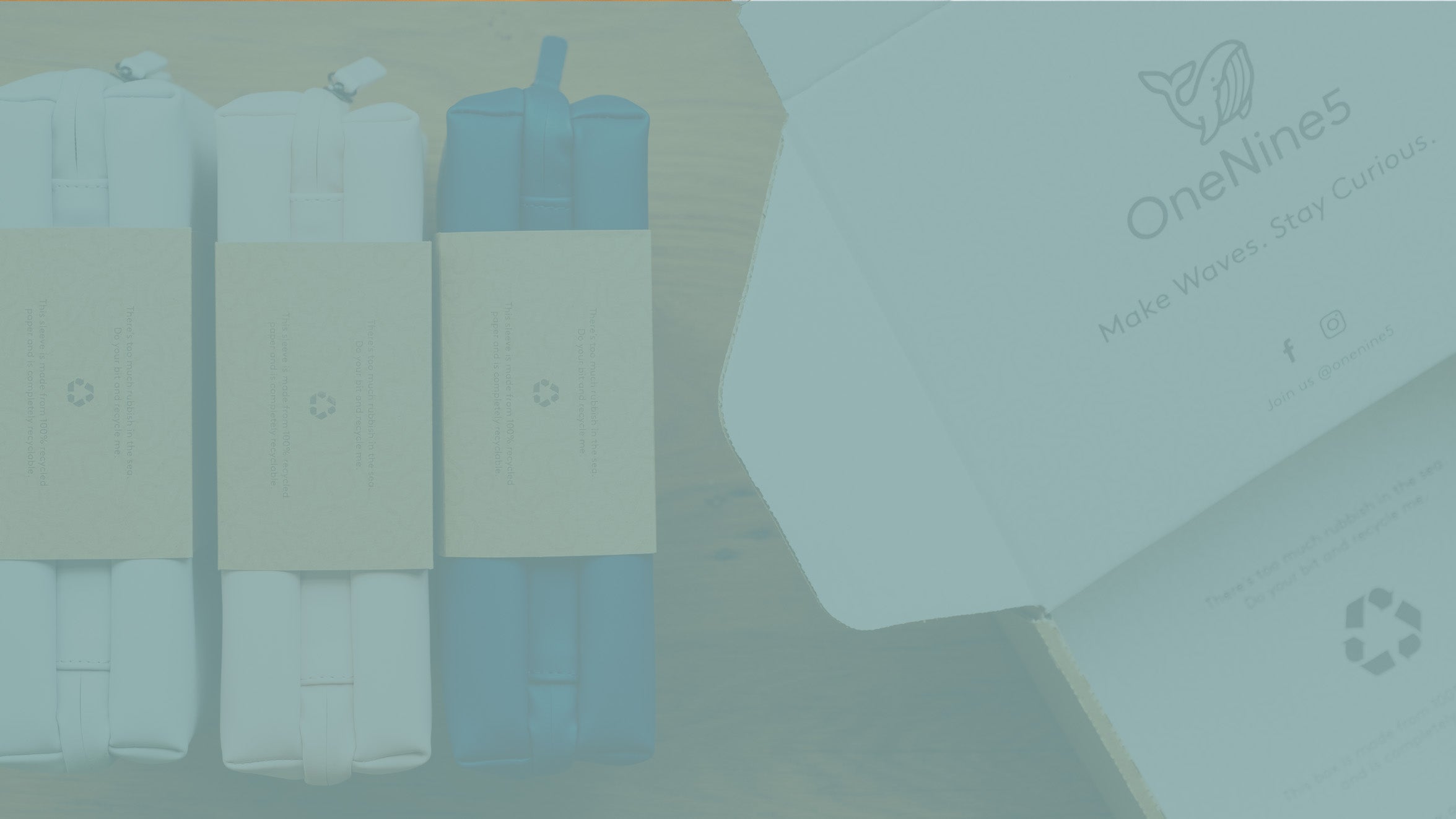 A birds-eye image of the OneNine5 wash bags in their recyclable kraft paper sleeves, next to an open and brand OneNine5 shipping box