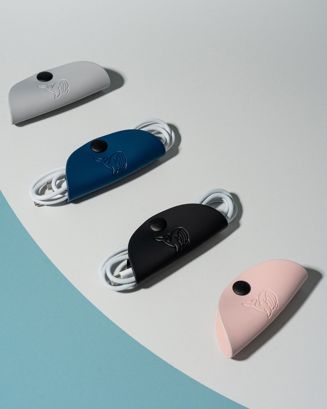 A black, blue, grey and pink OneNine5 cable tidy. Arranged neatly on a white and green background.