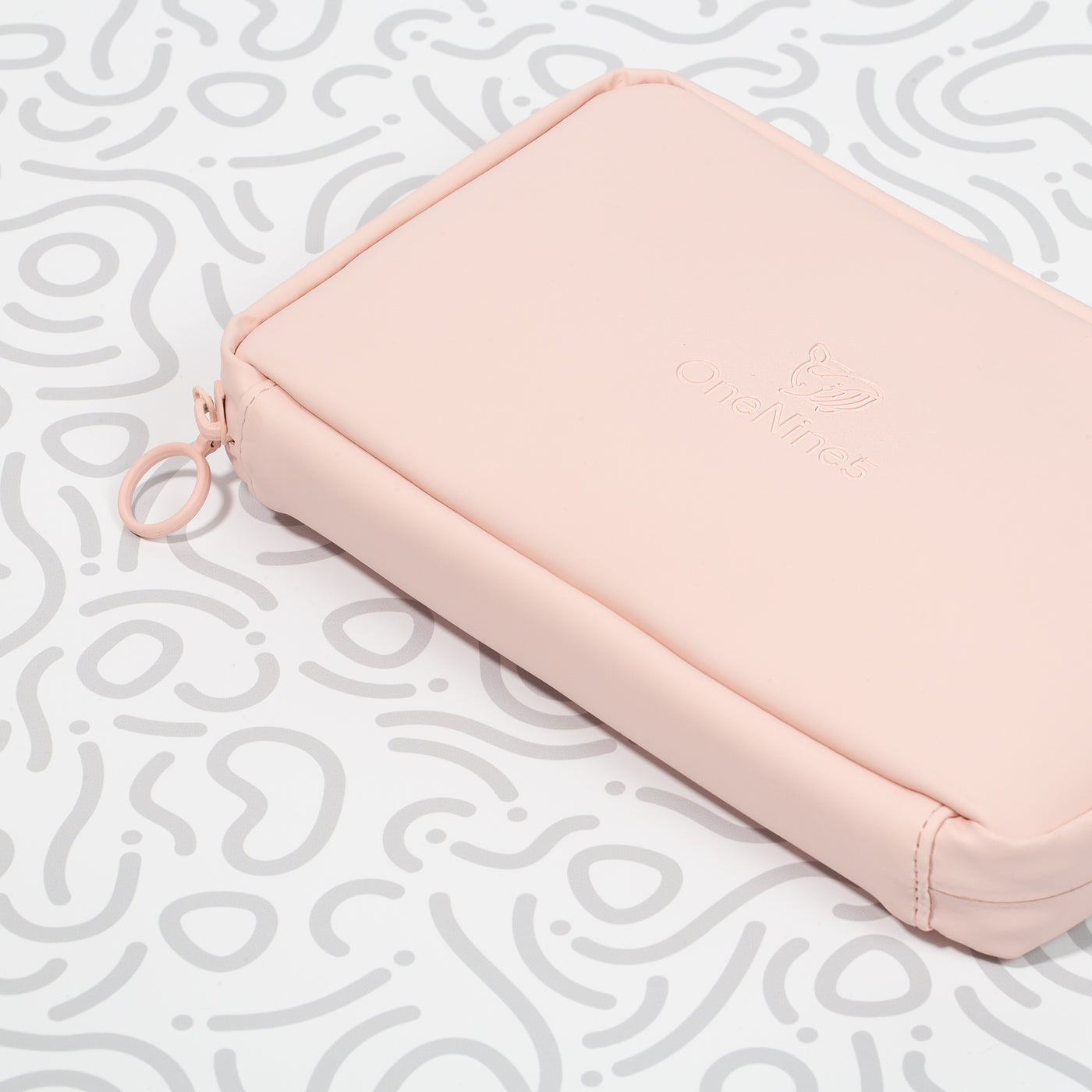 A closeup shot of the Komodo Pink Eco Essentials Pouch on a white background with the grey OneNine5 pattern. Close-up image shows detail of vegan leather outer, OneNine5 debossed whale logo, metal O-ring zip puller and pink stitching.