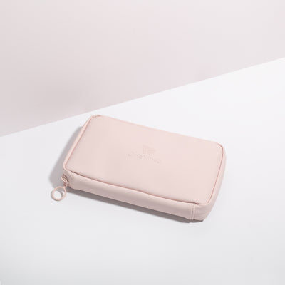 Komodo Pink Eco Essentials Pouch zipped closed and laid flat on a white surface, with a pink background behind. The angle of the image show’s the underside of the pouch. In the foreground, the metal O-ring zipper puller is visible on the left corner of the pouch.