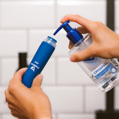 Female hands filling the wide neck of a blue OneNine5 silicone bottle with anti-bacterial hand sanitiser (gel)