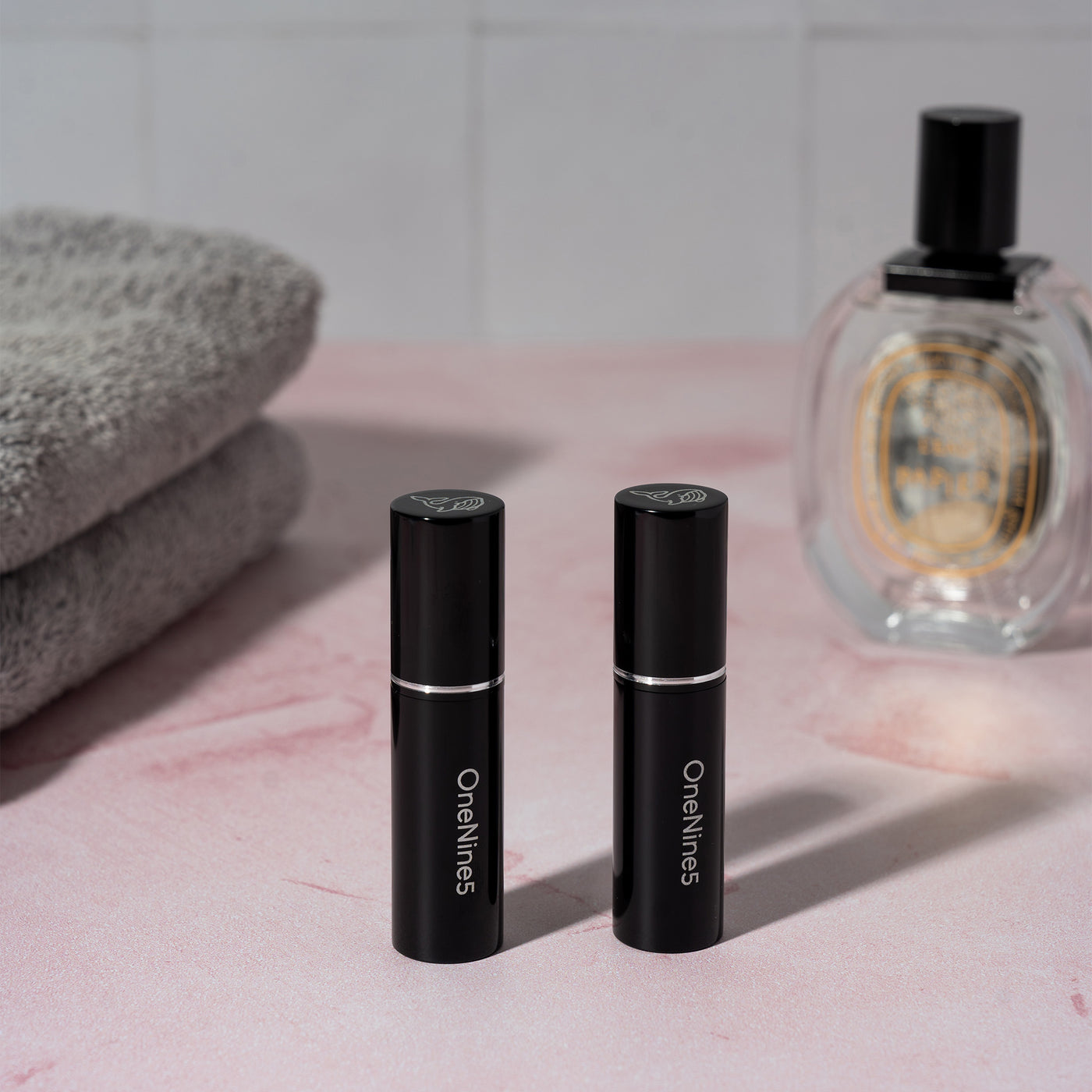 Two black OneNine5 refillable perfume & aftershave bottles. With towels in the background and a 100ml perfume bottle 