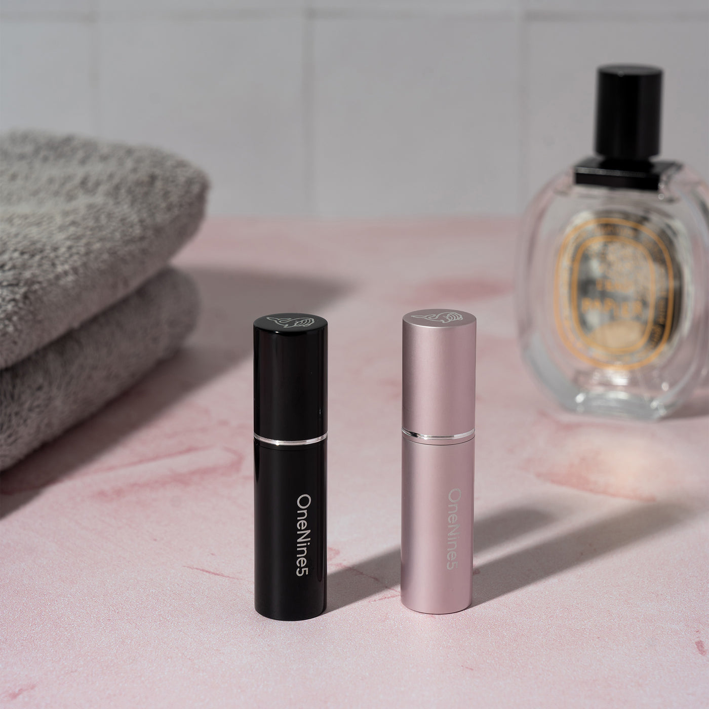 A black and pink OneNine5 refillable perfume/ aftershave bottle. With towels in the background and a 100ml perfume bottle