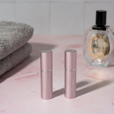 Two pink OneNine5 refillable perfume & aftershave bottles. With towels in the background and a 100ml perfume bottle