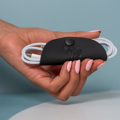 A female hand holding the black OneNine5 cable tidy with an Apple charging cable organised and coiled inside.
