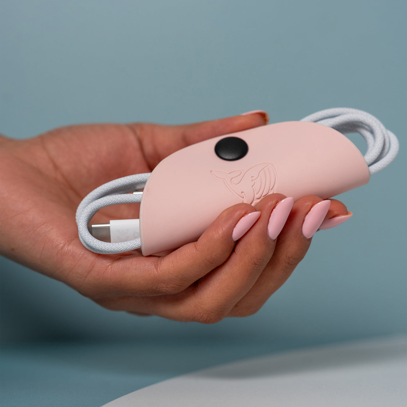 A female hand holding the pink OneNine5 cable tidy with an Apple charging cable organised and coiled inside.