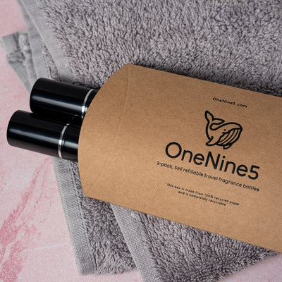 Two black OneNine5 fragrance bottles poking out of the natural kraft paper packaging, resting on a towel in the bathroom