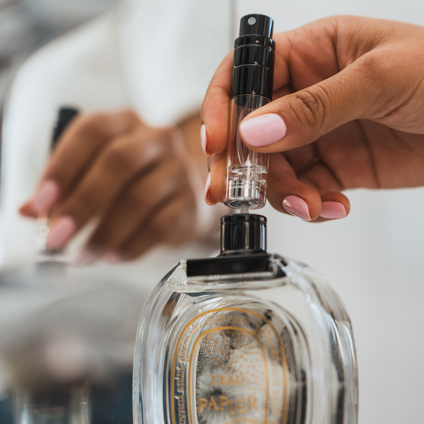 A female refilling the 5ml travel fragrance bottle in a bathroom. Pushing down on the leakproof pump to decant Diptyque 100ml fragrance into the 5ml travel bottle