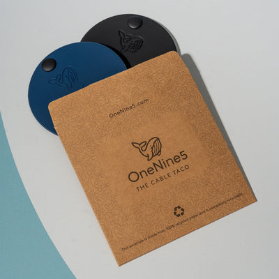 A black and blue OneNine5 cable tidy, poking out of the unbleached and plastic-free kraft paper packaging.