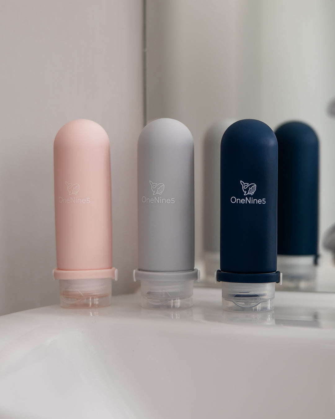 A pink, grey and blue OneNine5 silicone bottle, stood-up on a white porcelain sink in the bathroom