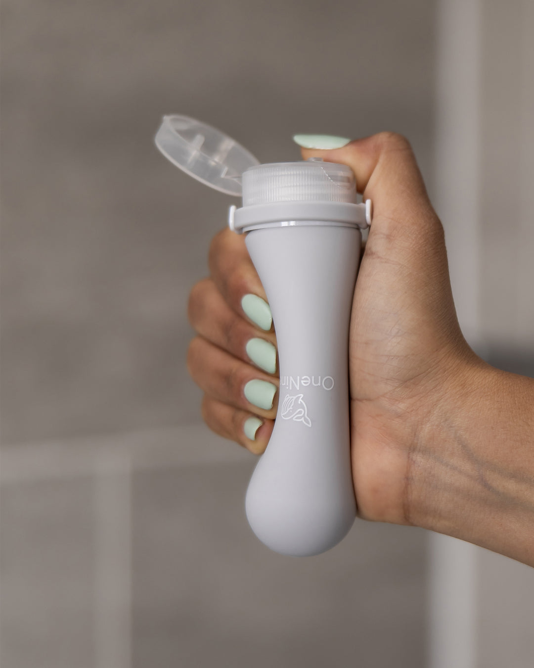 A female gripping and squeezing the soft silicone of a Moeraki Grey OneNine5 silicone bottle, with the cap flipped open