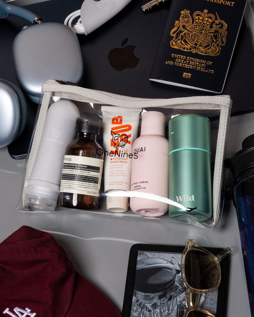 Travel-sized skincare products in a clear OneNine5 pouch, inside an airport security tray with other travel essentials