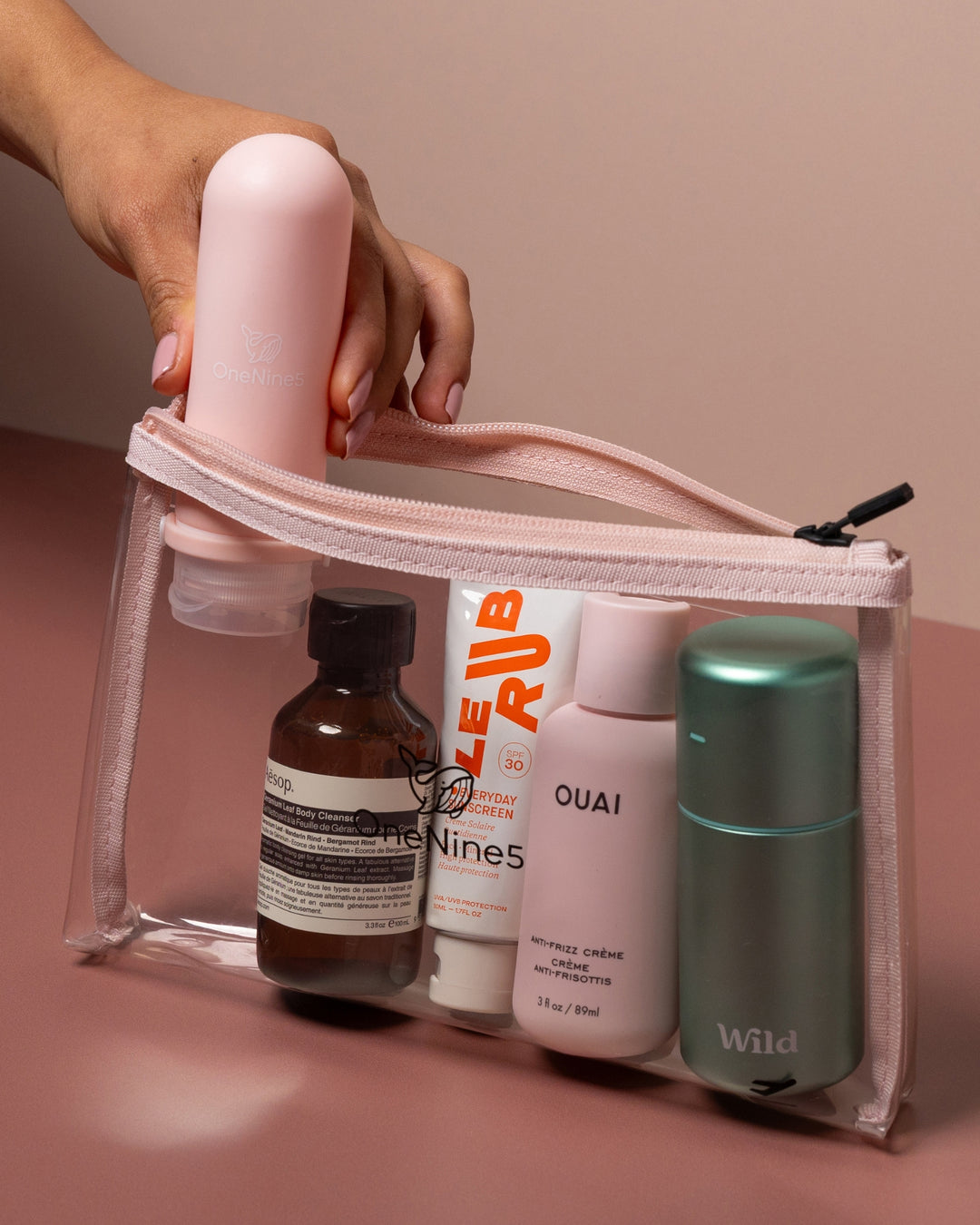 Clear travel pouch with cosmetic bottles on a pink background