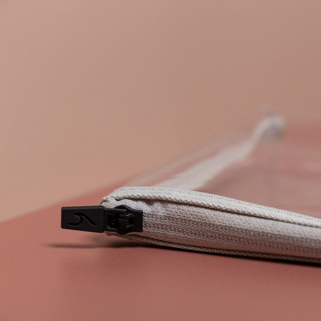 Close-up of grey clear liquid pouch zip with black debossed wave pull and textured fabric edge