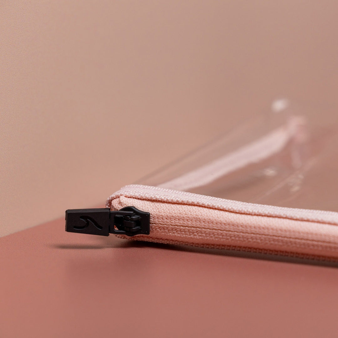 Close-up of pink clear liquid pouch zip with black debossed wave pull and soft fabric trim detail