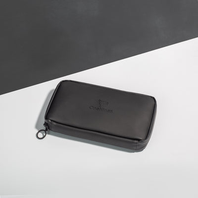 Miho Black Eco Essentials Pouch zipped closed and laid flat on a white surface, with a black background behind. The angle of the image show’s the underside of the pouch. In the foreground, the metal O-ring zipper puller is visible on the left corner of the pouch.
