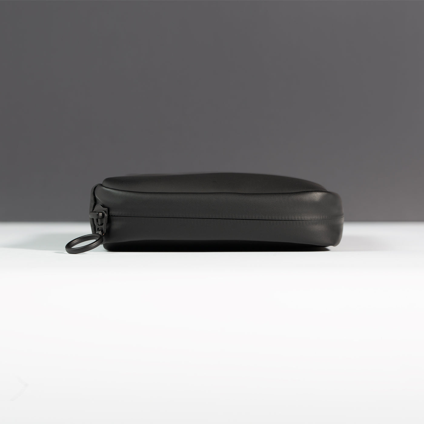 Side profile of the Miho Black Eco Essentials Pouch on a white surface with a black background. Image shows detail of outer black waterproof zipper tape and metal O-ring zip puller.