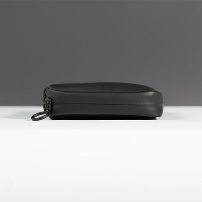 Side profile of the Miho Black Eco Essentials Pouch on a white surface with a black background. Image shows detail of outer black waterproof zipper tape and metal O-ring zip puller.