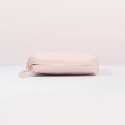 Side profile of the Komodo Pink Eco Essentials Pouch on a white surface with a pink background. Image shows detail of outer pink waterproof zipper tape and metal O-ring zip puller.
