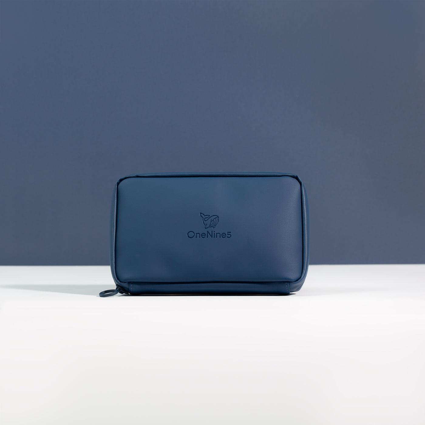 A front on view of the Havelock Blue Eco Essentials Pouch. Placed on a white surface with a blue background. The debossed OneNine5 logo is visible centrally on the front of the pouch.