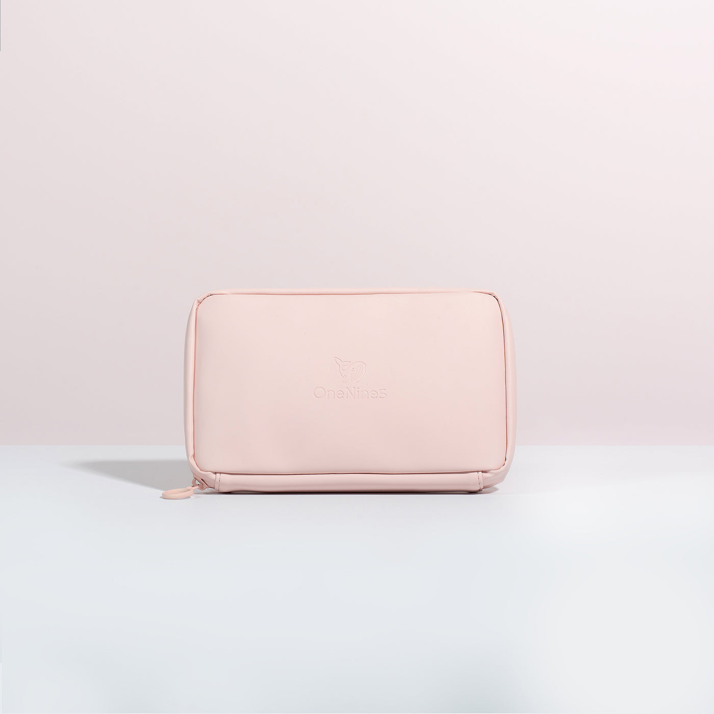 A front on view of the Komodo Pink Eco Essentials Pouch. Placed on a white surface with a pink background. The debossed OneNine5 logo is visible centrally on the front of the pouch.