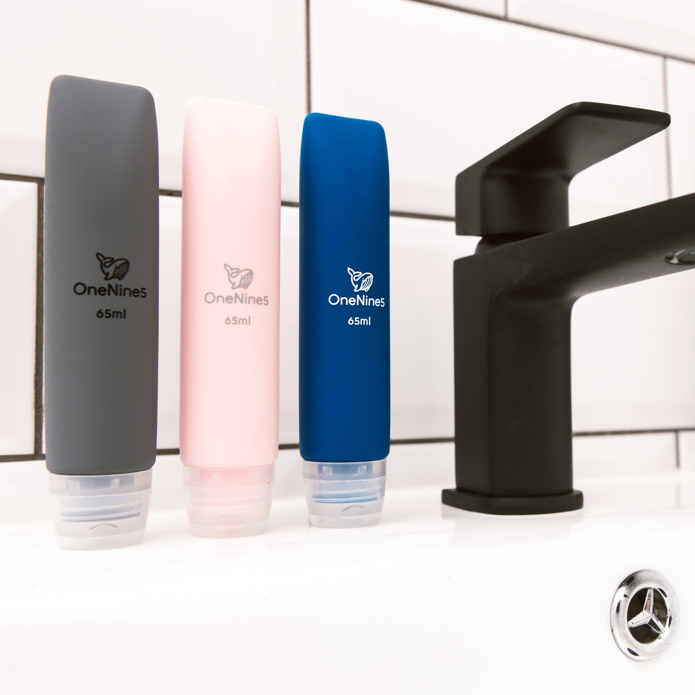 3 pack of OneNine5 mixed colour travel bottles on the bathroom sink, to the right of a black tap