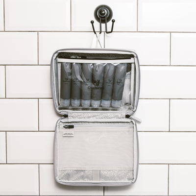 Six grey silicone travel bottles inside the clear toiletry pouch. The pouch is attached inside our OneNine5, Moeraki Grey wash bag using the hanging hook in the bathroom