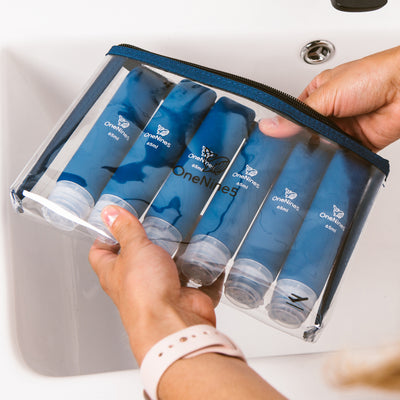 Women's hands holding six blue silicone travel bottles packed inside the removable OneNine5 toiletry/ cosmetic pouch.