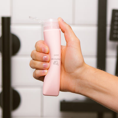 Female hand squeezing the soft silicone OneNine5 pink travel bottle, with the leakproof cap (lid) flipped open