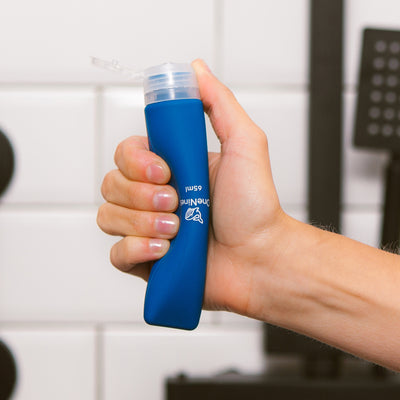 Women's hand squeezing the soft silicone OneNine5 blue travel bottle, with the leakproof cap (lid) flipped open