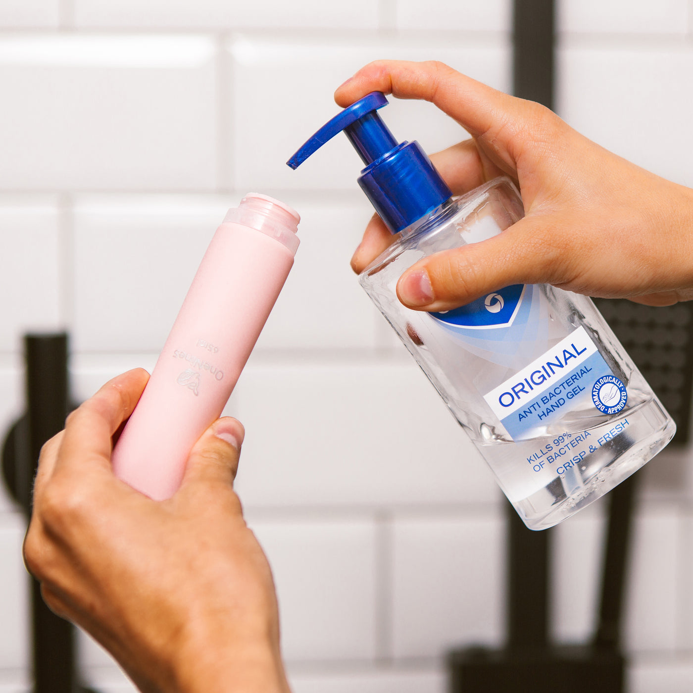 Female hands filling the wide neck of a pink OneNine5 silicone bottle with anti-bacterial hand sanitiser (gel)