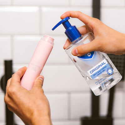 Female hands filling the wide neck of a pink OneNine5 silicone bottle with anti-bacterial hand sanitiser (gel)
