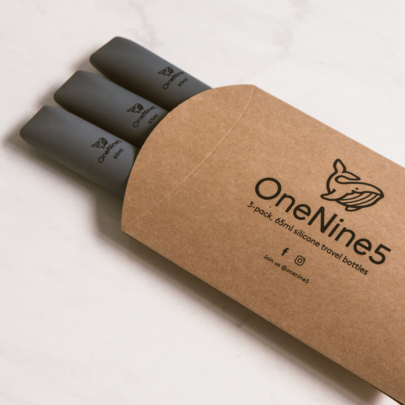 3 pack of grey silicone travel bottles are packed inside brown, recyclable kraft paper. The packaging is branded with a black OneNine5 logo 