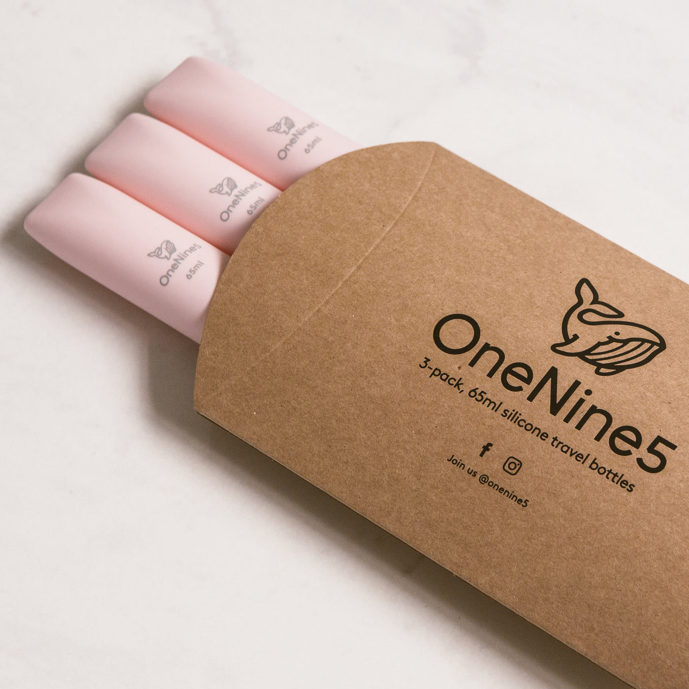 3 pack of pink silicone travel bottles are packed inside brown, recyclable kraft paper. The packaging is branded with a black OneNine5 logo