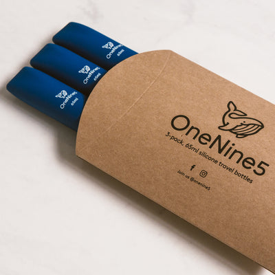 3 pack of blue silicone travel bottles are packed inside brown, recyclable kraft paper. The packaging is branded with a black OneNine5 logo