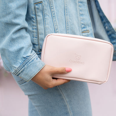 A female wearing a blue denim jacket and blue denim jeans is holding the Komodo Pink Eco Essentials Pouch in her right hand, down by her waist. She is stood in front of a pink shop.